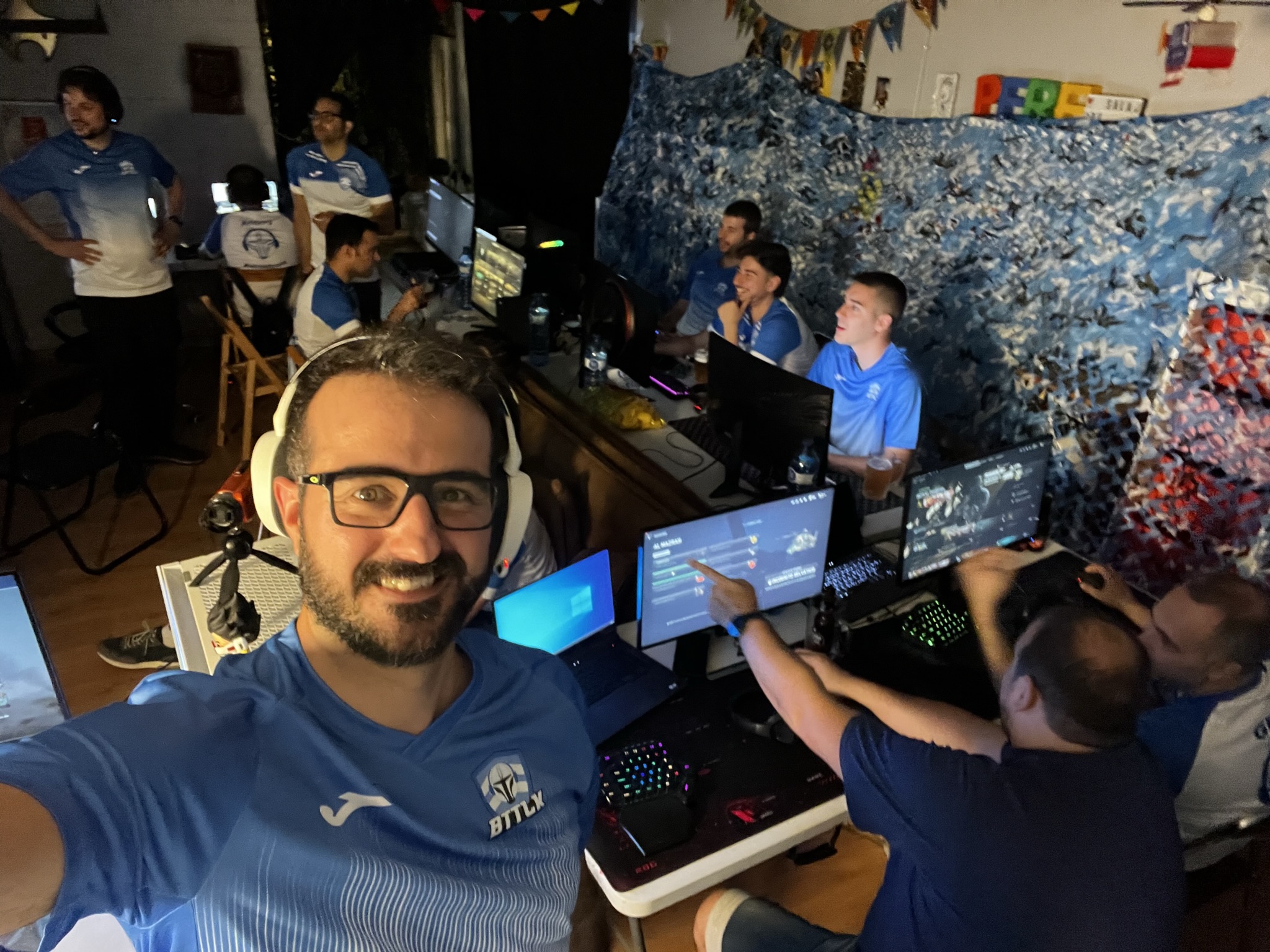 Selfie en la LAN party con los auriculares puestos, monitores encendidos al fondo